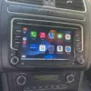 Dashboard of the Volkswagen Polo Cross featuring a touchscreen display with various app icons, including maps and music. Below the screen, there are manual controls for radio and climate settings, along with a digital clock display.