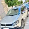 A silver Volkswagen Polo Cross parked on a city street, with a tree and buildings in the background, surrounded by other vehicles.