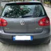 A gray Volkswagen Golf 5 2.0 TDI is parked on a paved street, with trees and buildings visible in the background. The car's license plate is partially obscured.